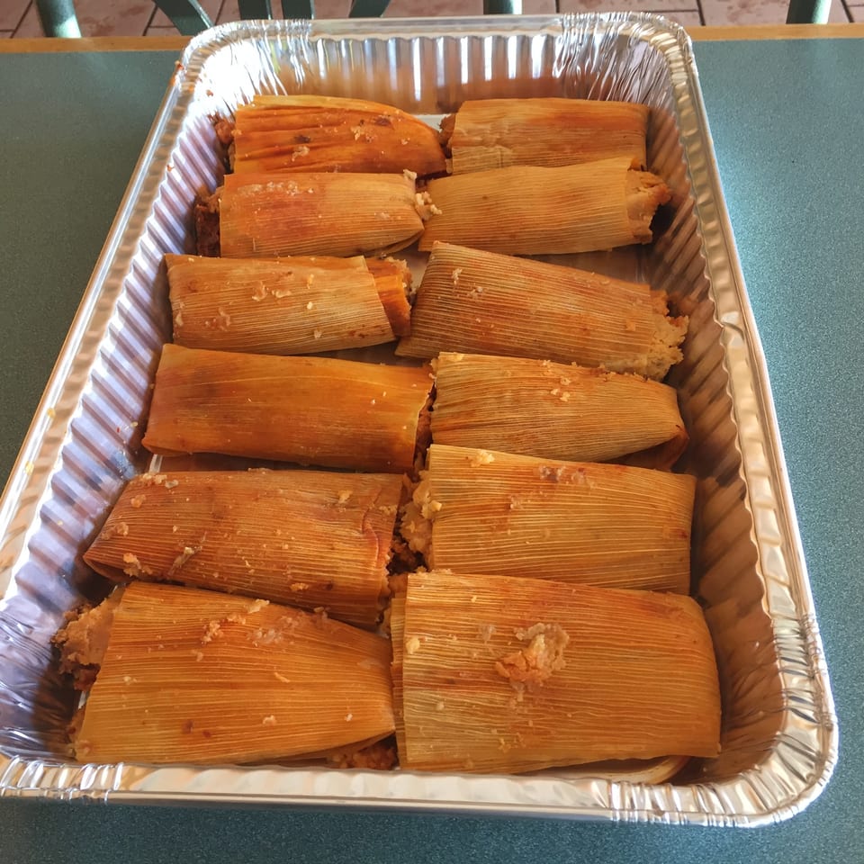 A foil pan filled with many freshly made tamales, some slightly open to show the filling.
