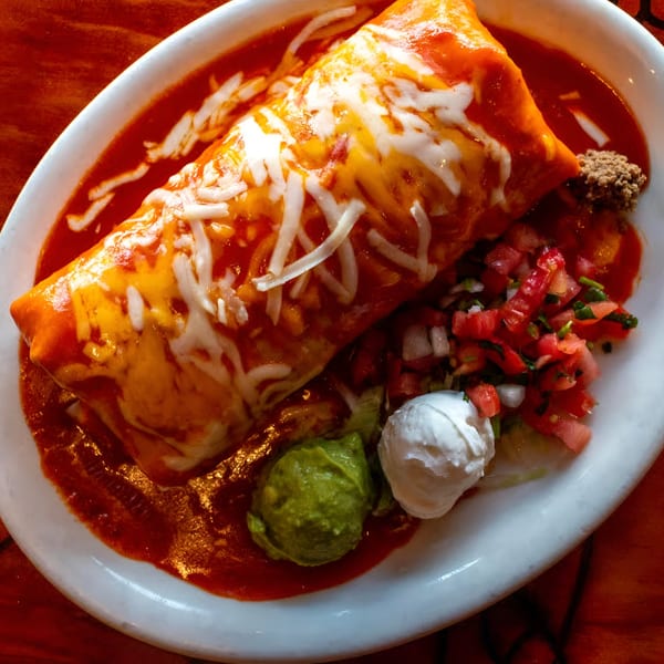 A large, cheese-covered burrito smothered in red sauce, with guacamole, sour cream, and pico de gallo.