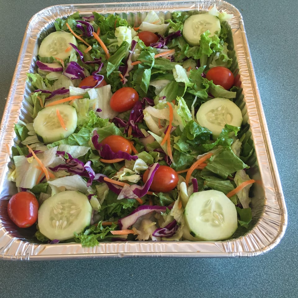 A large foil tray filled with a fresh garden salad, including lettuce, cucumbers, tomatoes, and carrots.