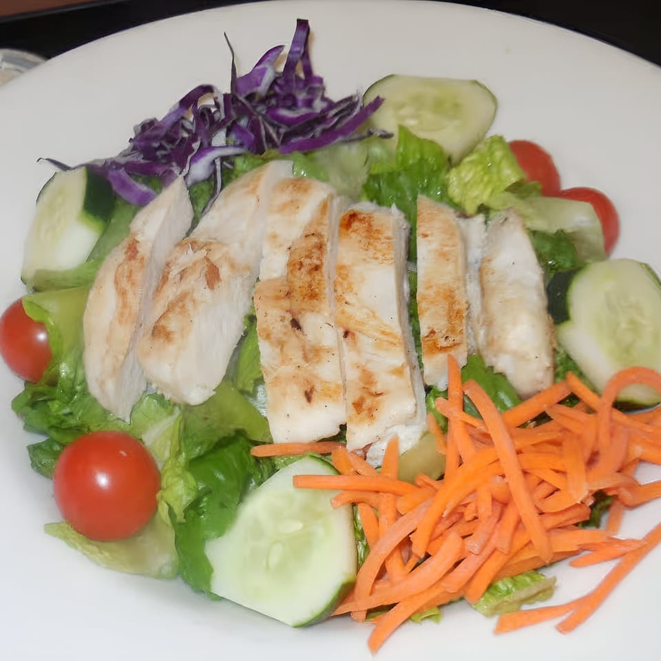 Grilled chicken salad with lettuce, red cabbage, cucumbers, cherry tomatoes, and shredded carrots.