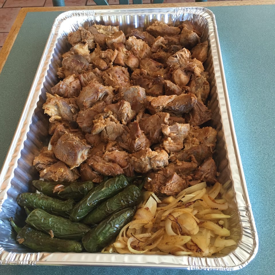 A large foil pan filled with seasoned pork, roasted green chiles, and caramelized onions.