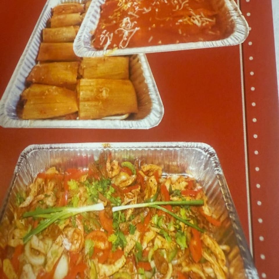 Three foil trays of Mexican food: tamales, enchiladas, and a stir-fry with shrimp and vegetables.