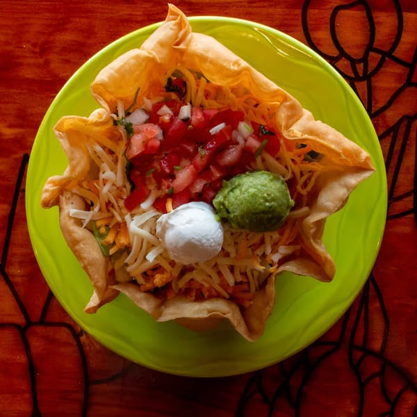 A taco salad in a crispy tortilla bowl with pico de gallo, guacamole, and sour cream.