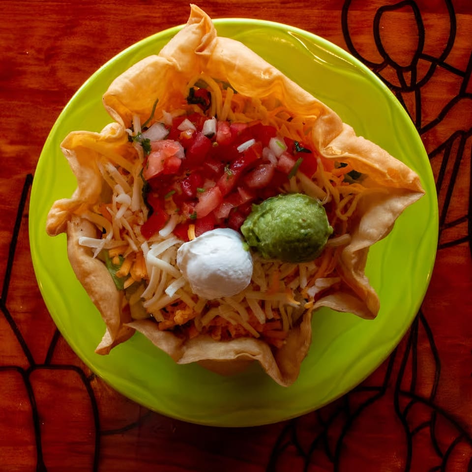 A taco salad in a crispy tortilla bowl with pico de gallo, guacamole, and sour cream.