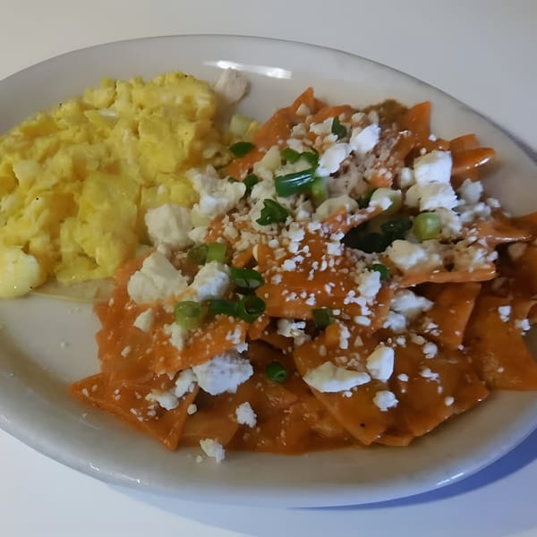 Chilaquiles with red sauce, crumbled cheese, green onions, and a side of scrambled eggs.
