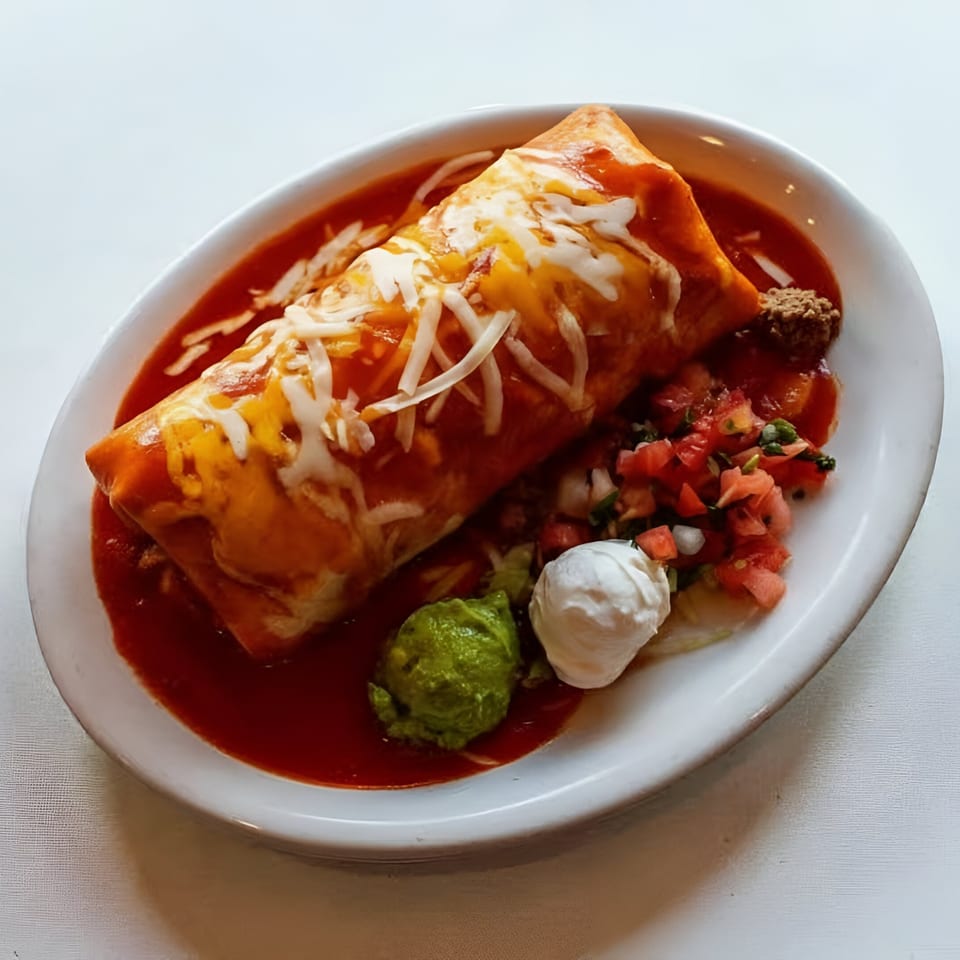 A large, cheese-covered La Fuente Mexican Restaurant burrito in red sauce, with guacamole, sour cream, and pico de gallo.