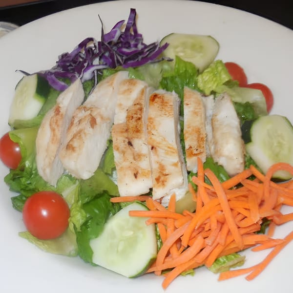 Grilled chicken salad with lettuce, shredded carrots, cucumbers, cherry tomatoes, and red cabbage.